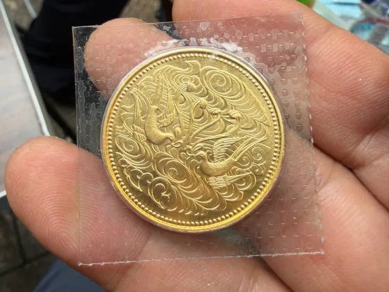 透明の袋に入った御在位60年記念10万円金貨の鳥を配した図柄の面