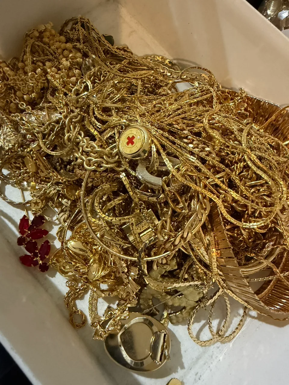 白い容器にまとまった金色のチェーンや輪状のアクセサリー、赤い装飾の付いたイミテーションアクセサリー